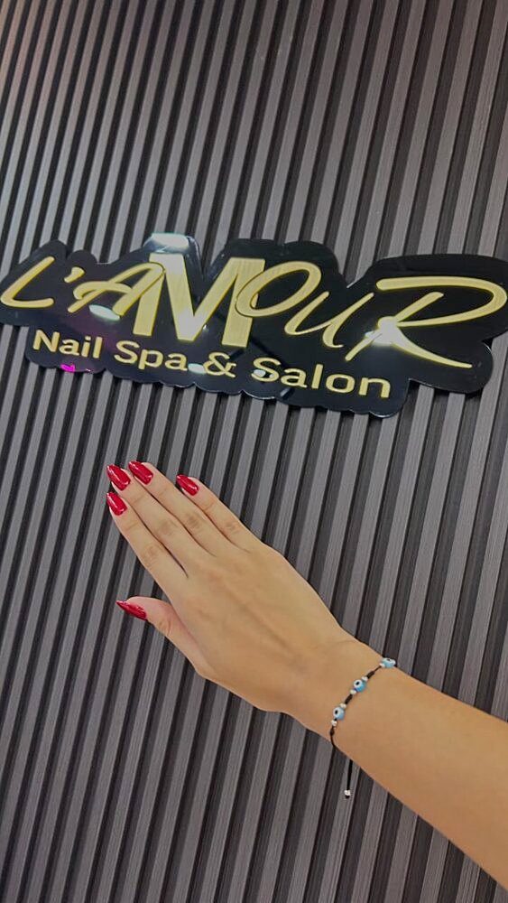Manos con uñas rojas frente al letrero de L'Amour Nail Spa & Salon